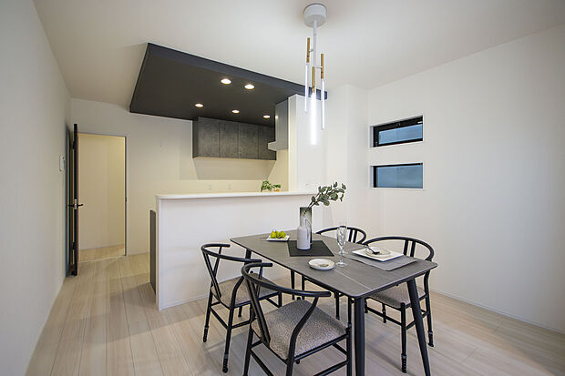 【【LDK】】リビングをすっきりと見渡せる対面式キッチン。キッチン部分はダークカラーのポップアップ天井を採用しており、空間のアクセントに。メリハリのある雰囲気を演出しています。