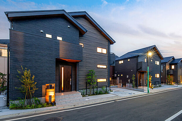 【【　住協建設の施工例　】】黒の木目調が織りなす重厚な佇まい。 洗練されたダークトーンの質感が夕暮れの街並みに美しく映える、デザイン性の高いモダン邸宅。