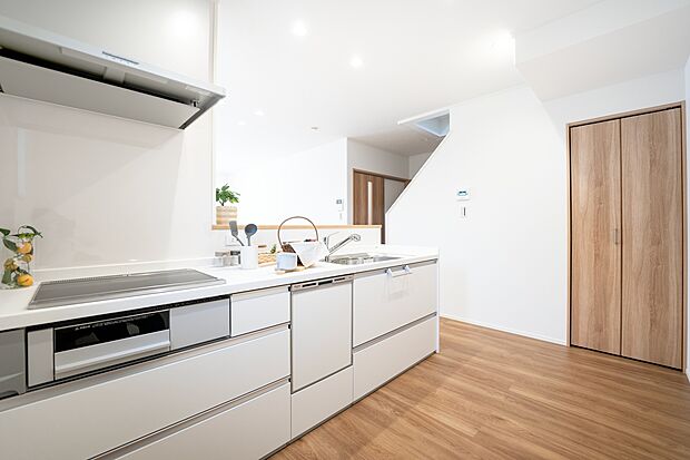 【1階キッチン/B号地】IHクッキングヒーターは使用後のお手入れがしやすいフラット形状。正面に壁を設けることで、ダイニングへの油跳ねを防ぎます。リビング階段下スペースを活用し、収納を設けています。