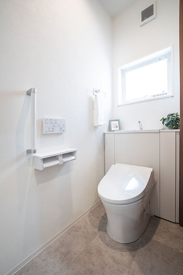 【【1階トイレ/A号地】】1年を通して快適な温水洗浄便座付きです。タンクが視界に入らず、スッキリとした見た目に。壁面の操作パネルは楽な姿勢で利用でき、立ち座りをサポートする手すりを備えています。