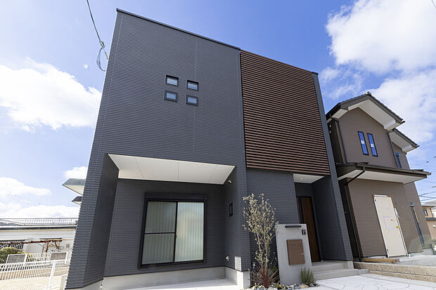 【【外観/当社施工例】】洗練された雰囲気を醸し出す、キューブ型のスタイリッシュな外観です。木目のルーバーと玄関扉が温もりをプラス。街並みと調和する、いつまでも飽きのこない住まいに。