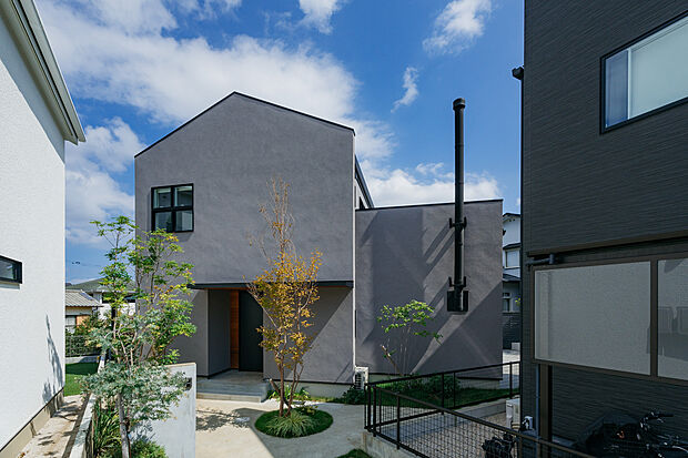 【塗り壁と煙突が魅力のあたたかな佇まい】グレーの塗り壁と印象的な煙突が目を引く、上質な外観デザイン。植栽とのバランスも良く、四季の変化を楽しめる落ち着いた住まいです。