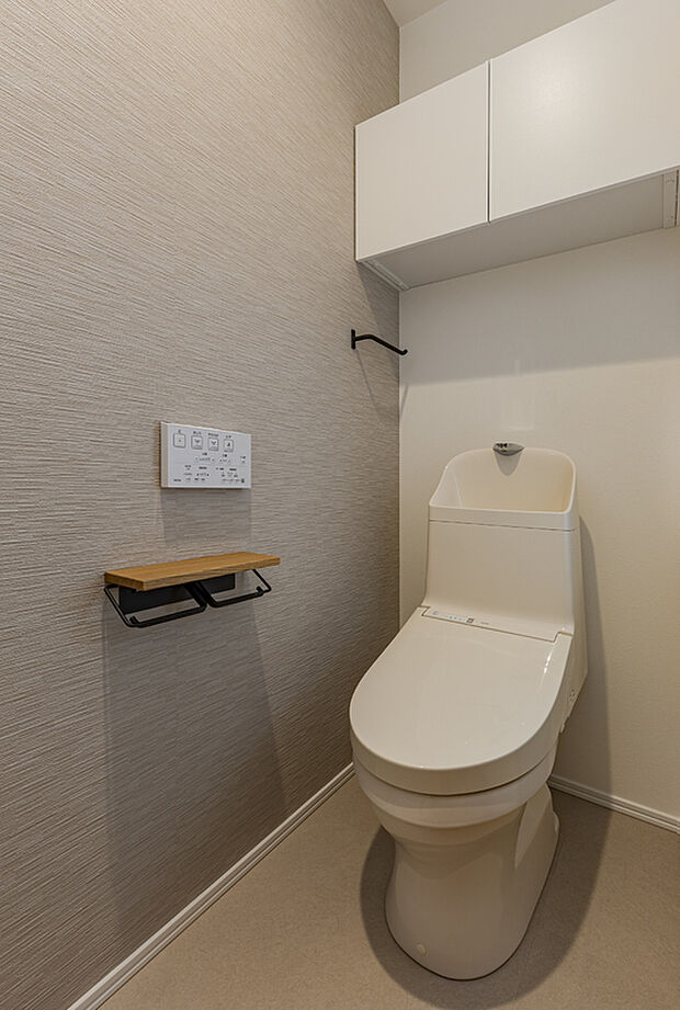 【【トイレ/当社施工例】】グレーのアクセントクロスがお洒落な佇まい。年間を通して、快適に使うことができる温水洗浄便座付き。リモコンは操作しやすい壁付けタイプ。上部には収納を設置しました。