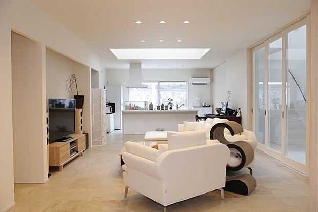 【建物プラン例(内観写真)】玄関扉を開けると、真っ白な大空間が広がっています。清潔でさわやかな印象だけでなく、色彩の効果で空間がより一層大きく感じます。玄関を一歩入ると、真っ直ぐに伸びる吹き抜け廊下のエントランスを挟んで、東西に間取りが大きく構成されています。西側は応接間を兼ねた10数畳の土間のサロンが配置され、その北側は段差を設け、家族がくつろぐLDKに。仕切り戸もあるので2部屋の独立が可能です。水回りはLDKの北側にまとめました。/当社施工例