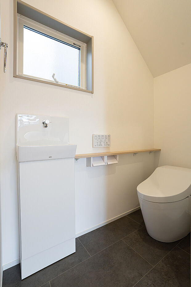 【トイレ】すっきりとした空間に仕上げた、タンクレストイレ。 タンクレスの便器を採用することで、トイレ内を広くすっきりと見せています。手洗い器を独立して設け、使いやすさにも配慮。壁面にはカウンターを設け、ペーパー類などを置ける実用的なスペースに。