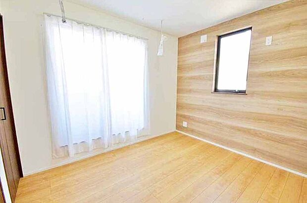 【洋室】フローリング床と木目のアクセントクロス、掃出し窓と小窓で自然光が入る居室です。