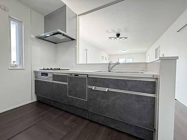 【9号棟 キッチン】ダークトーンの石目調パネルが空間を引き締める、対面キッチン。リビングを見渡せる設計で、お料理中も家族との会話が楽しめます。洗練された調理空間。