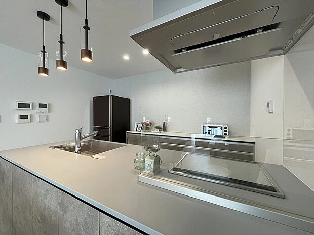 【5号地キッチン】
石目調のやさしい質感が印象的なキッチン。コンロ前はガラスパネルで開放感を保ちつつ油はねをガード。背面収納と色味を揃え、すっきりとした統一感のある空間です。