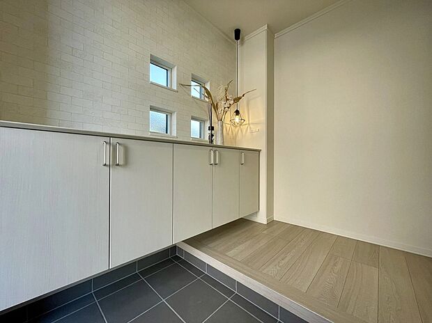 【玄関】白を基調としたアクセントクロスと広々カウンターが印象的な玄関。小窓からの光で明るく、お気に入りの小物や花も楽しめます。吊り下げ収納で掃除もしやすく、気持ちよく一日を始められる空間です。