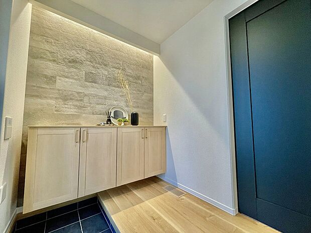 【2号地　玄関】玄関を開けると、間接照明のやわらかな光に包まれた上質な空間。壁面の表情を美しく引き立て、奥行きと広がりを演出します。フロート収納で足元もすっきりし、ホテルのような落ち着きと心地よさを感じられます。