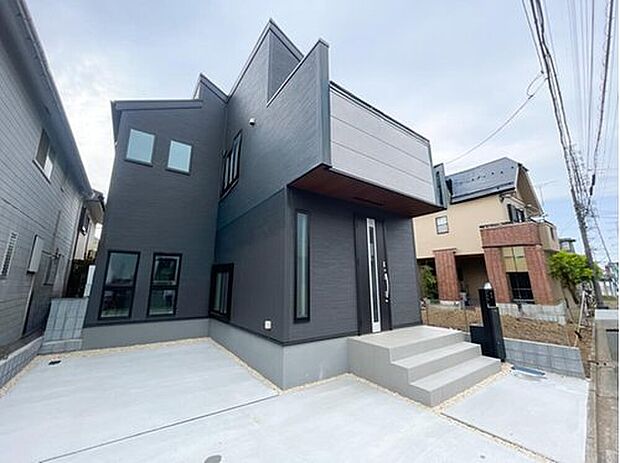 【現地外観写真】凹凸のあるフォルムが都会的な、デザイナーズ住宅のような外観。重厚感のあるダークトーンに、玄関ポーチの木目調が温かみを添えます。高いデザイン性とプライバシーへの配慮を両立させた、誇らしい佇まいです。