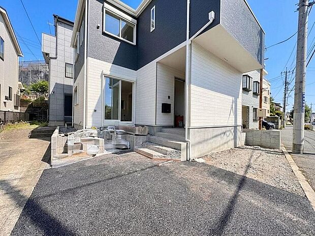 【現地外観写真】白とダークグレーのコントラストが美しい、洗練された外観デザインの住まい。明るい陽光が降り注ぐアプローチは、家族の笑顔を迎える場所。新しい暮らしがここから始まります。