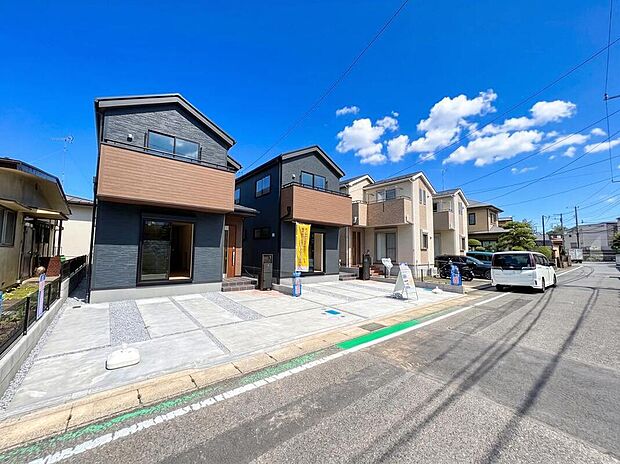 【前面道路含む現地写真】閑静な住宅街に佇む、シンプルな外観デザインの2邸。濃い色合いをベースに、ナチュラルカラーを組み合わせることで、モダンな印象の中に温もりをプラスしています。