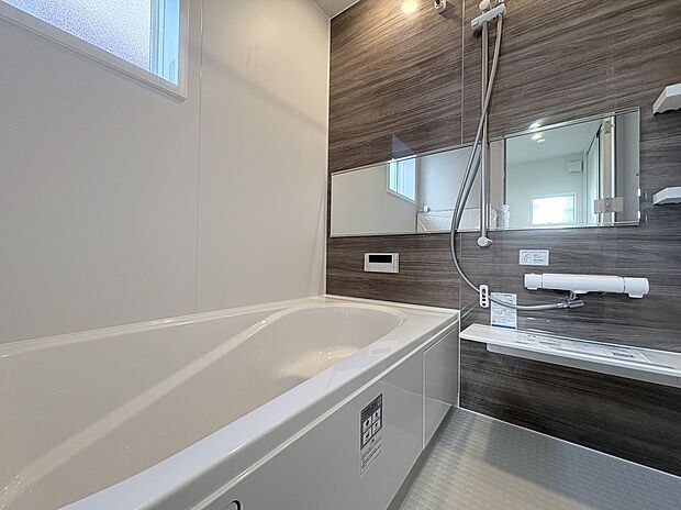 【浴室　A号棟現地写真】■リクシル　システムバスルーム「AX」。フロアはスポンジが奥まで入り掃除がラクラク。また独自の断熱層を使用しているため冬場でも冷やっとしません。