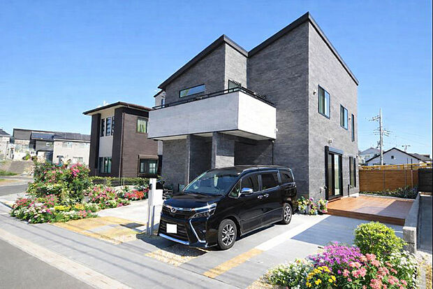 【外観（施工例）】重厚なグレー外壁と迫力のバルコニー、開放的なウッドデッキが魅力の邸宅。