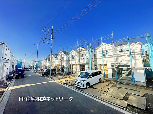 【現地外観写真】青空に映える白い街並みが広がり、完成へ向けて工事が順調です。広い道路で駐車もスムーズ。全体として明るく開放的な雰囲気の閑静な住宅街が形成されています。
