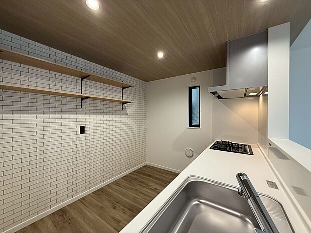 【カフェ風のお洒落なキッチン】白いレンガ調の壁と木目天井が温もりを添える、棚付きカウンターキッチン。るでカフェのような落ち着きと上質な雰囲気を演出。毎日の料理が、ちょっと特別なひとときに変わります。