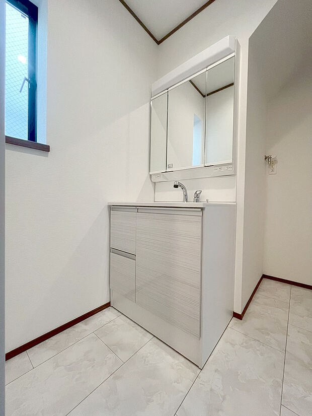 【三面鏡仕様の洗面化粧台を備えた洗面室】3号棟～ゆとりの洗面スペースで朝の身支度も快適スムーズに。三面鏡で髪のセットやお化粧もストレスなくこなせ、朝から気分良く通勤通学に向かえそうですね！鏡の裏にはたっぷりと収納スペースを標準装備！