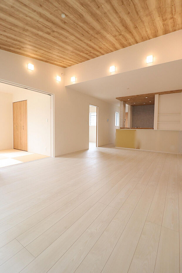 【LDK(19帖)】 木目天井と照明が調和した、ナチュラルで温もりのある住空間。一般的なクロス天井とは異なる、こだわりを感じる印象的なLDKに仕上がっています。