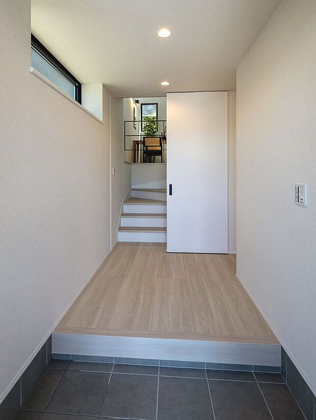 【玄関】光が差し込む玄関から始まる、木目の温もり感じる心地よい空間。上へと続く階段の先に、家族の笑顔が待つプライベートな時間が広がります。