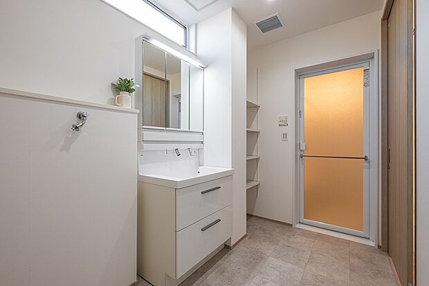 【収納充実で使いやすい明るい洗面脱衣室】三面鏡収納と可動棚を備えた、使い勝手の良い洗面脱衣室。朝の支度や洗濯動線をスムーズにし、家事の負担を軽減します。採光窓のある明るい空間です。