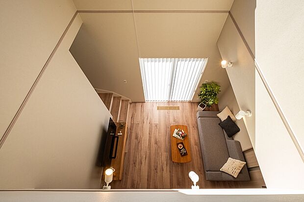 【吹き抜けが生む明るさと開放感あるリビング】吹き抜けから降り注ぐ光がリビング全体を包み、広がりを感じる心地よい空間です。階段・窓の配置により、家族の動きが自然とつながる一体感のある間取りになっています。