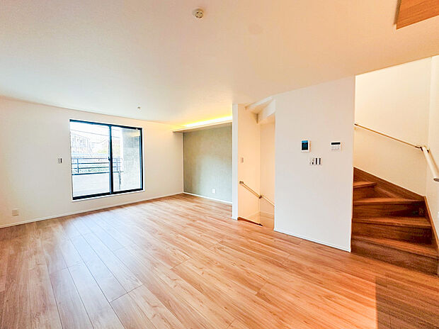 【リビング】広々としたリビングダイニングは、明るいフローリングと白壁を基調とし、空間の広がりを感じさせます。壁際の間接照明と、モダンなアクセントクロスが落ち着いた雰囲気を演出。