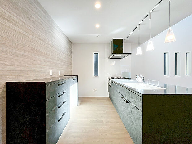 【キッチン】キッチン本体と背面収納を同色で統一し、壁面の木目調アクセントが高級感を演出。大容量の収納スペースで、生活感を感じさせない洗練された空間をキープし、心地よいキッチンタイムを実現します。