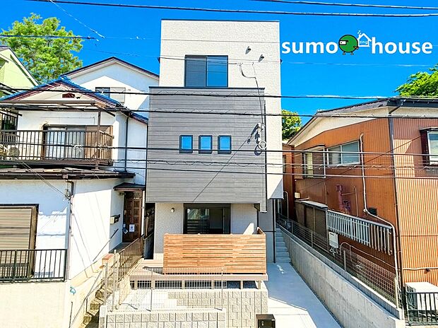 【洗練されたデザイン】白とグレーのタイル調外壁を組み合わせた都会的なデザインが、周囲の街並みの中でも一際個性を放ちます。プライバシーに配慮したウッド調の目隠しフェンスは、デザインのアクセントとしても機能。