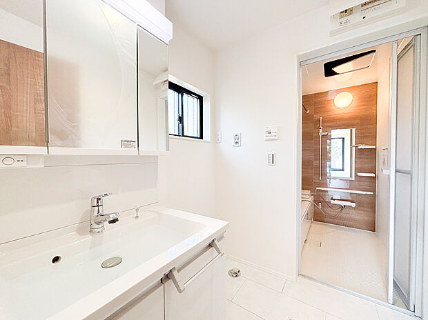 【洗面化粧台】白を基調とした清潔感あふれる洗面室には収納付き三面鏡を備えた機能的な洗面台を採用しました。鏡の裏に小物をスッキリ収納できるため、常に整った空間を保てます。ハンドシャワー付きで日々のお手入れも快適です。