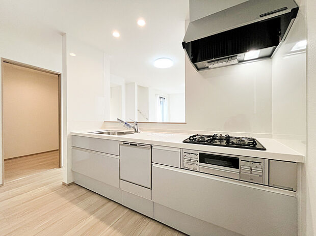 【システムキッチン】白を基調とした清潔感あふれるシステムキッチン。家事効率を高めるビルトイン食洗機や3口コンロを完備しています。リビングを見渡せる対面式で、家族との会話を楽しみながらお料理ができる開放的な設計です。