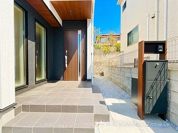 【長期優良&耐震最高等級のデザイナーズ住宅】モダンで落ち着いた色調が印象的な玄関アプローチは、住まいの顔として上質な品格を演出しています。また、不在時にも重宝する宅配ボックス付きの機能門柱を完備しており、共働き世帯にも嬉しい仕様となっています。