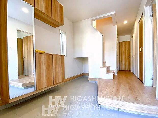 【建物プラン例 (内観写真)】施工例(玄関)収納力とデザイン性を兼ね備えた玄関空間。家族全員の靴も収まるシューズボックス付き。大きな姿見で、お出かけ前のチェックもスムーズ。玄関ホールには自然光が入り、明るく清潔感ある印象に。