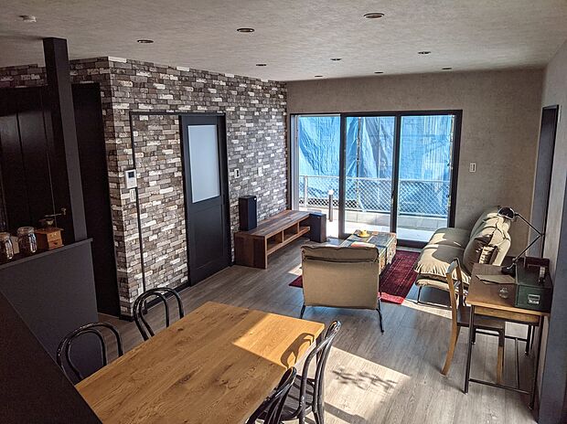 【無骨な素材感が映えるLDK参考画像（インダストリアルハウス）】レンガ調クロスやダークトーンの素材が映える無骨で洗練されたLDK。大きな窓から自然光が差し込み、重厚感と明るさが調和した居心地の良い空間です。