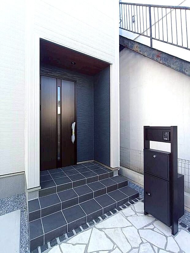 【玄関】シックなドアと木目調の軒天がお洒落な玄関。手前にはインターホンやポスト、不在時にも荷物を受け取れる便利な宅配ボックス付きの機能門柱がスマートに設置されています。