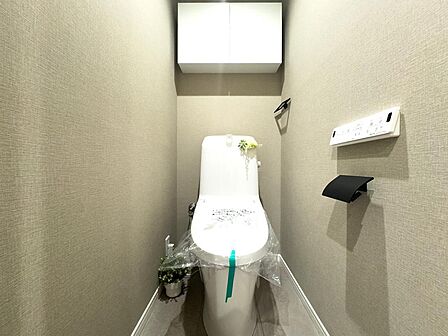 「新規交換済みの快適トイレ」 温水洗浄機能付きのトイレに新品交換済み。上部には便利なペーパー類のストック用吊戸棚を配置。シックなアクセントクロスが落ち着いた雰囲気を演出します。