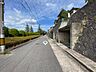 その他：青い空と緑の植栽が広がる、開放感のある道路です。車庫付きの建物も確認でき、暮らしやすさが期待できます。