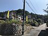 外観：緑豊かな山を背景にした、閑静な住宅街の一角。青空が広がる明るい現地写真です。