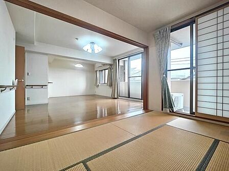 畳敷きの和室とフローリングの洋室が隣接しており、引き戸を開放することで一体感のある空間として活用できる間取りです。壁面には手すりが設置されているほか、バルコニーへ出られる大きな窓を備えています。