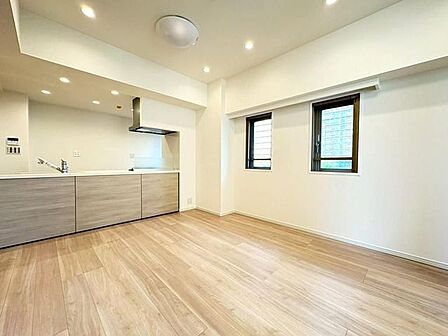 木目調のカウンターパネルを採用した対面式キッチンを備えたリビングで、ナチュラルな木目調フローリングや壁面に並ぶ2つの小窓、天井に配置されたダウンライトなどの設備が整っています。