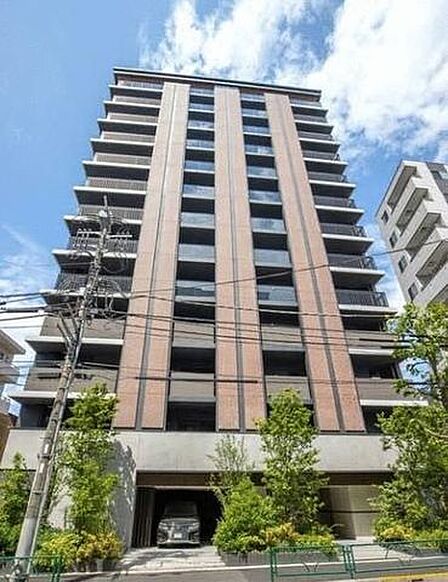 ブラウンとグレーを基調としたシックなカラーリングの外観デザインで、1階部分には植栽が施されており、建物内には駐車スペースも配置されています。