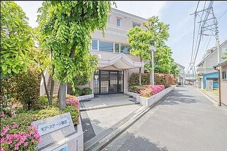 淡いピンク系のタイル貼りの外壁デザインが特徴的な建物で、エントランスアプローチの沿道には緑豊かな植栽や花壇が配されており、屋根付きのガラス戸エントランスへとフラットに続いております。