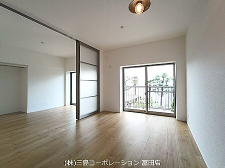 明るい光が差し込むリビングは、木目調の床と白い壁が調和し、心地よい空間を演出しています。可動間仕切りで空間をフレキシブルに活用できます。