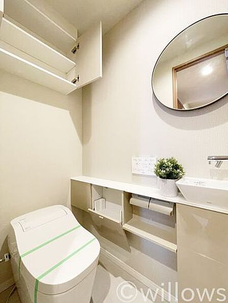 おしゃれな丸鏡や専用の手洗いカウンターを備えた、上質でホテルライクなトイレスペースです。上部にはトイレットペーパーや掃除用品などを隠してしまえる収納棚も設置されており、清潔感のある空間を保てます。
