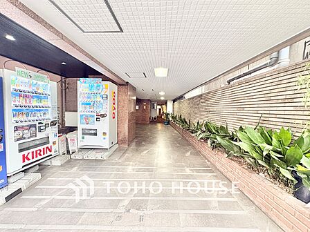 通りから一歩入ったアプローチには丁寧に手入れされた植栽が並び、住まい手や訪れる人を心地よく迎えてくれます。自動販売機も設置されており、日常のちょっとした便利さも嬉しいポイントです。