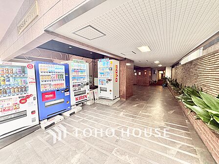 通りから一歩入ったアプローチには丁寧に手入れされた植栽が並び、住まい手や訪れる人を心地よく迎えてくれます。自動販売機も設置されており、日常のちょっとした便利さも嬉しいポイントです。