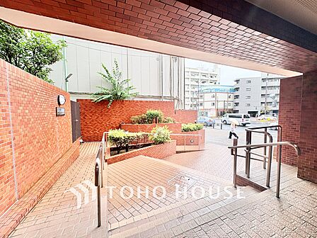 緑豊かな植栽と手すり付きスロープを配した開放的なアプローチ。奥まで見通しが良く、防犯面でも安心感のある設計です。