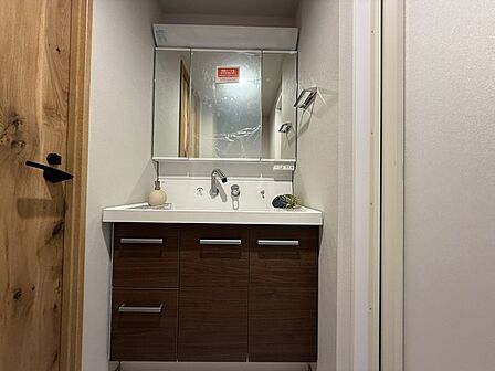 洗面室は明るく清潔感のあるコンパクトな空間です。 大きな三面鏡と照明が使いやすく、収納も充実。 シンプルで機能的なデザインが魅力です。