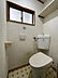トイレ：窓と収納棚を備えたトイレです。温水洗浄機能付き便座が設置され、日用品を置ける棚もあるため、実際の使い勝手を確認できます。日々の清掃にも配慮できます。※AIによる家具消し加工を行なっております。