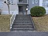 エントランス：丁寧に手入れされた植栽が優しく出迎えるエントランスは、住まう人の品格を感じさせます。手すり付きの階段が設けられた安心の設計で、毎日を健やかに支える細やかな配慮が随所に散りばめられています